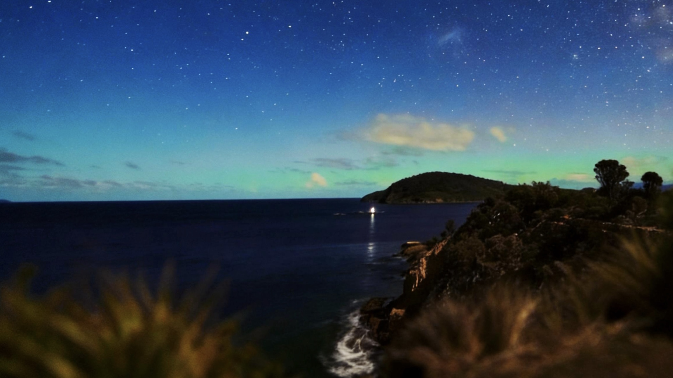 星空下的海岸与远处山丘,深蓝海面上有一点灯光